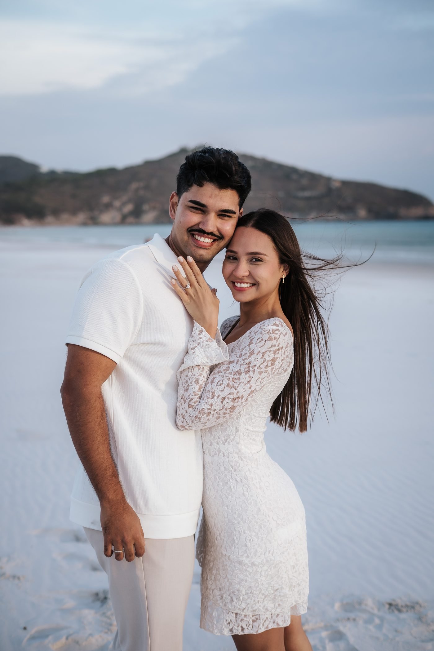 Mariana e Théo abraçados na praia, os dois de branco